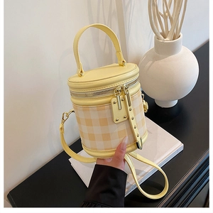 Close-up of quilted cylinder bucket bag in yellow and beige with top handle and strap