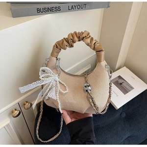 Detailed close-up of woven beige hobo bag featuring lace and pearl bow charms and chain strap