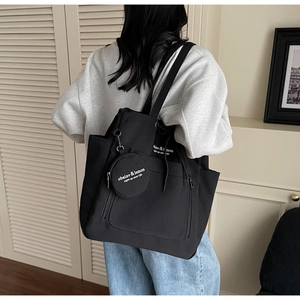 Detail of a large black canvas tote bag with front zipper pocket and round mini pouch