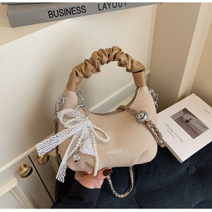 Detail of beige woven handbag featuring lace bow, pearl charms and brown pleated handle