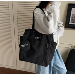 Close-up of black canvas tote bag with round coin purse charm and white text print