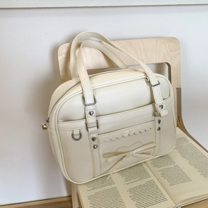 Detail of cream Boston bag with heart rivets, scalloped edges, and bow decoration