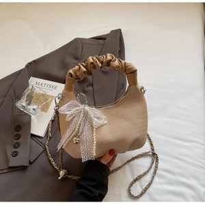 Detailed shot of woven beige handbag with lace bow, pearl fringe and leather chain strap