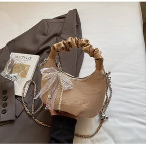Detail of khaki moon bag with pearl lace bow and silver chain strap on art book background