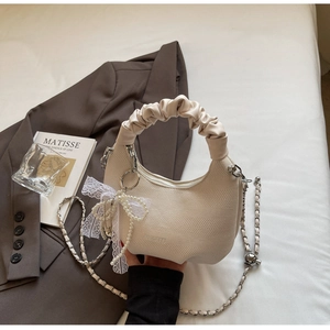 Detail of cream knit crescent bag featuring pearl bow charm and pleated handle
