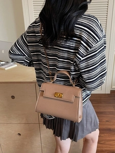 Chic beige leather crossbody bag with gold twist lock and chain strap on a desk