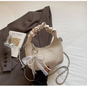 Detailed view of cream crescent bag with woven texture and pearl lace bow accessory