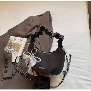 Close-up of black knit texture handbag with white lace bow and pearl charm detail