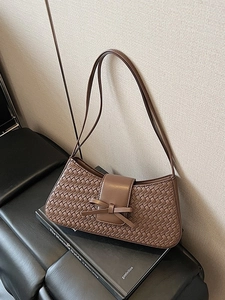 Minimalist woven dark brown underarm bag with decorative leather bow on beige background
