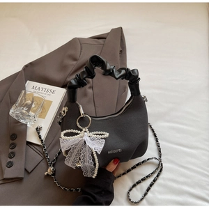 Detail of black textured handbag featuring cloud pleat handle and pearl lace bow charm