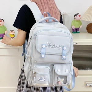 Détail du sac à dos en toile bleu clair avec plusieurs poches et lettrage décoratif