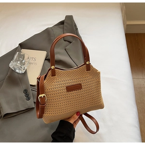 Detail of hand-woven straw bucket bag with dark brown leather handles and gold metal hardware