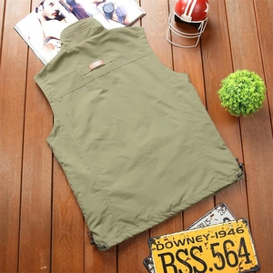 Flat lay of an olive green outdoor utility vest with drawstring hem on a wooden floor