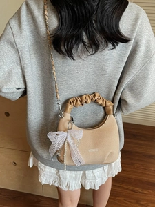 Beige knit dumpling handbag with lace bow and chain strap shown on a model