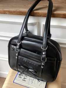 Elegant black JK style tote bag with heart hardware and bow on a rustic wooden chair