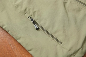Close-up of olive green vest featuring ripstop fabric and woven puller zipper pocket