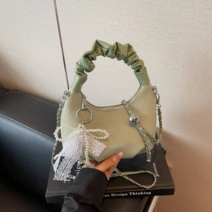 Sac hobo vert tissé avec nœud en dentelle de perles et chaîne argentée sur sofa noir