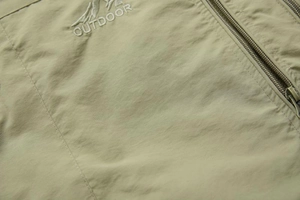 Detailed close-up of khaki outdoor vest fabric with embroidery and double metal zippers