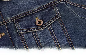 Gros plan d'une veste en jean bleu foncé avec surpiqûres orange et détail de bouton bronze