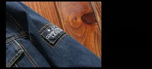 Detail of dark blue denim jacket featuring contrast stitching and vintage embroidery patch