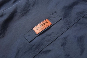 Detail of a navy blue casual vest featuring a classic brown leather patch with stitching