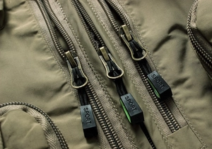 Macro view of olive green tactical vest featuring three parallel zippers with Sport logo tags