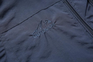 Detail of navy blue outdoor vest featuring mountain embroidery and durable zipper texture