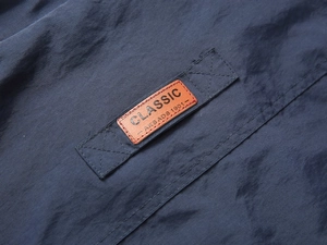 Detail of navy nylon fabric with a stitched brown classic leather logo patch on a vest