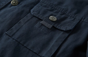 Détail macro d'une veste bleu marine montrant une poche boutonnée et des coutures précises