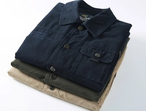 Détail de vestes d'extérieur empilées en coton marine, vert olive et kaki avec broderie