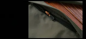 Close-up of olive green outdoor jacket featuring a black zipper with orange woven puller