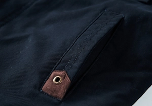 Detailed macro shot of navy twill fabric with brown suede patch and metal eyelet detail
