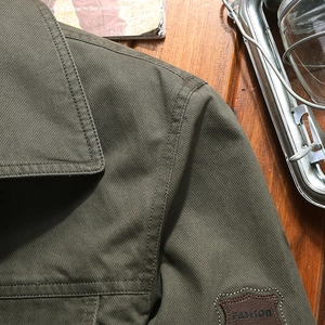 Olive green cotton workwear jacket with leather patch details on a rustic wooden desk