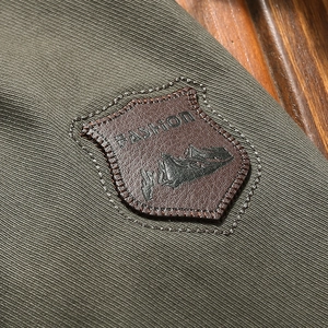 Army green cotton casual jacket detail featuring a leather mountain emblem on olive fabric