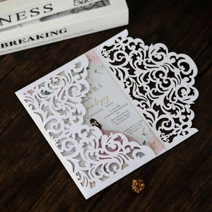 Laser-cut white wedding invitation with elegant floral insert on dark wooden desk