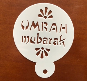 Macro detail of PET cake stencil with Umrah Mubarak cutout design on dark wood