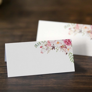 Segnaposto nuziali floreali con rose acquerellate su tavolo in legno scuro