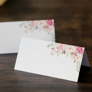 Dettaglio macro di segnaposti bianchi con eleganti rose rosa su tavolo in legno