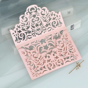 Detail of laser-cut pink wedding invitation with intricate scroll pattern on pearl paper
