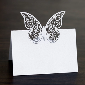 Macro shot of laser-cut butterfly place cards on a dark wood texture for wedding parties