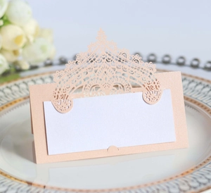 Detail of laser-cut wedding name place card with hollow crown pattern on a dinner plate