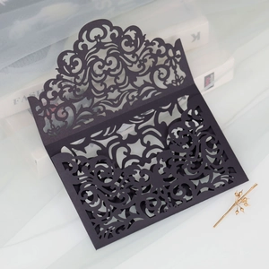 Macro shot of laser-cut black wedding invitation featuring intricate vine and floral patterns