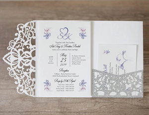 Detailed laser-cut wedding invitation set with floral card on a rustic wood surface