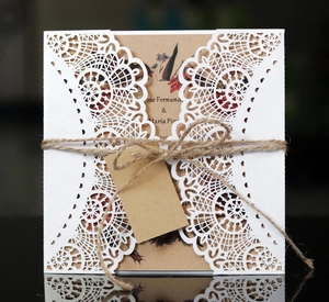 Detail of laser-cut white lace invitation with kraft paper insert and jute twine