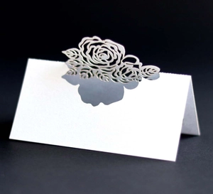 Detail of white laser-cut place card with rose pattern for wedding table decor