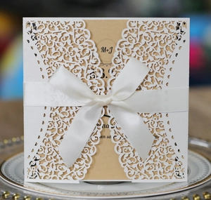 Detailed laser-cut hollow wedding invitation with white satin bow and ornate floral patterns