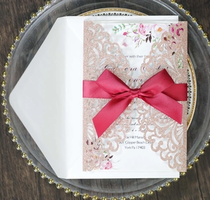 Dettaglio invito nozze oro rosa glitter con fiocco di raso rosso e inserto floreale