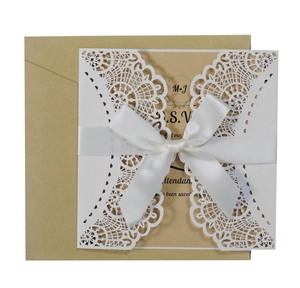 Detail view of laser-cut lace wedding invitation with white ribbon bow and kraft insert