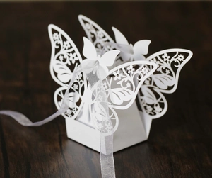 Detailed laser-cut hollow white wedding favor box with butterfly top and satin ribbon