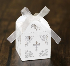 Detail of white laser-cut cross candy box with rose patterns and organza ribbon
